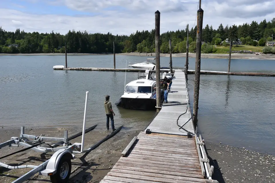 Animated sequence: an Explorer 24 hovercraft flies from the water onto its ground deployment trailer on a low tide beach, is secured, and is towed away