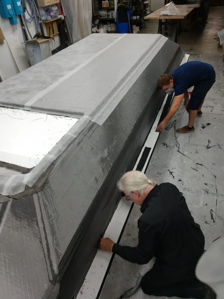 Two builders laying carbon and glass fabric over an Explorer 24 hull