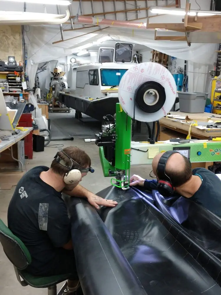 Two builders hot air welding a hovercraft skirt in the shop