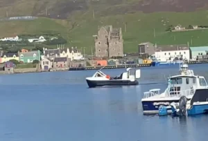 Mark's Explorer 22 crossing a Shetland harbour past fishing boats and a castle ruin