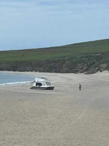 Mark's Explorer 22 on a wide empty sand beach below green hills