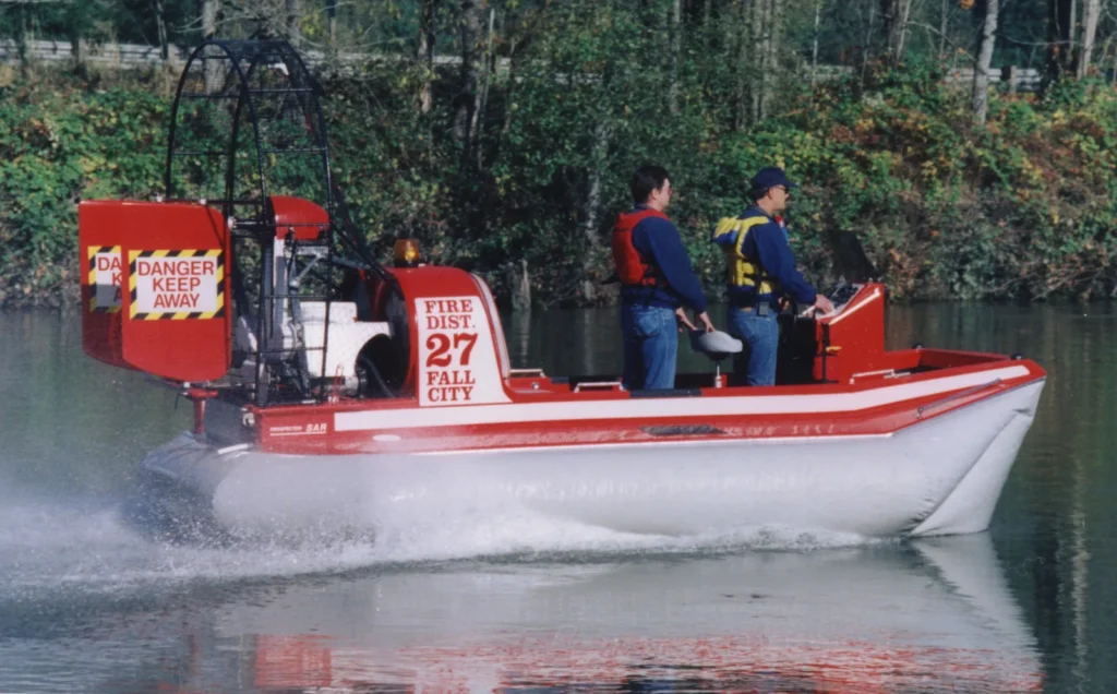 Two firefighters in life jackets running the Prospector rescue hovercraft on a river
