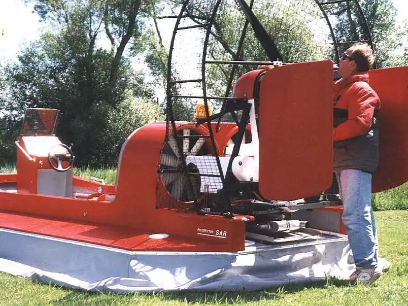 The red Prospector SAR hovercraft on a lawn with a builder standing beside it