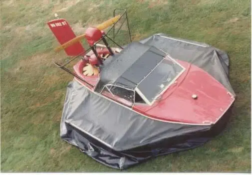 The red molded fiberglass Sevtec hovercraft with its cover on, parked on grass