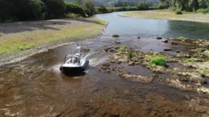 Surveyor 16 hovercraft crossing rocky river shallows, throwing spray, seen head on