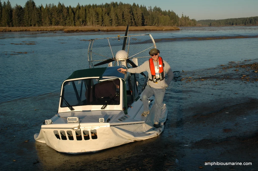 Bryan Phillips standing beside a Vanguard hovercraft at the water's edge